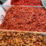 A pile of red shrimp sits in a white container, ready to be cooked.