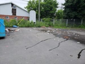 A pile of trash is sitting in a parking lot, with a sign nearby.