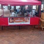 A red tent with a sign that says "Sabor & Cia" is set up on a brick walkway.