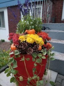 A red vase filled with flowers and plants sits on a step.