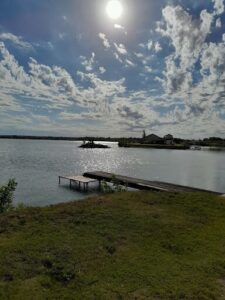 A serene scene of a lake with a pier and a house in the background.
