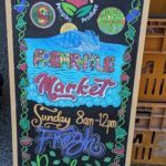 A sign advertising a market is displayed on a wooden board.