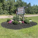 A sign for Farmer Brown's Greenhouse is displayed in front of a greenhouse.
