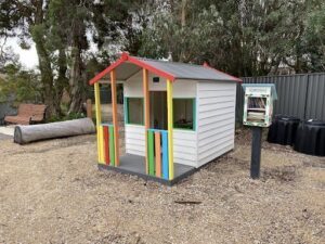 A small, colorful shed sits in a dirt field.