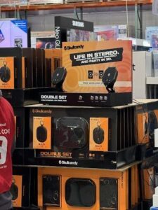 A stack of Skullcandy products, including a double set of speakers, sit on a shelf.