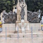 A statue of a woman holding a shield is located in the middle of a city.