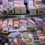 A variety of cheeses are displayed in a store, including cheddar, gouda, and brie.