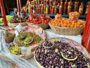 A variety of fresh vegetables are displayed in baskets, including peppers, tomatoes, and oranges.