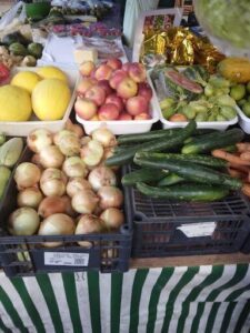 A variety of fruits and vegetables are displayed in baskets and crates, including apples, onions, and cucumbers.