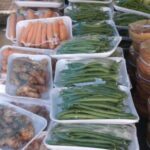 A variety of vegetables are displayed in plastic containers, including carrots, green beans, and other assorted vegetables.