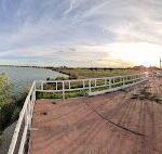 A view of a pier with a fence and a bridge over the water.