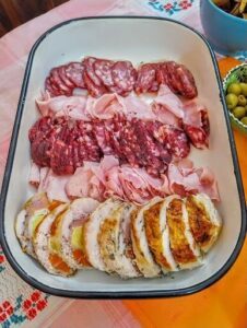 A white bowl filled with a variety of meats and olives.