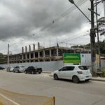 A white car is driving down a street in front of a construction site.
