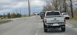 A white truck is driving down a road with a line of cars behind it.