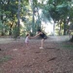 A woman and a little girl are playing together in the woods.