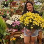 A woman is holding a bouquet of yellow flowers, smiling and posing for the camera.