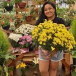 A woman is holding a yellow flower in a brown paper bag.