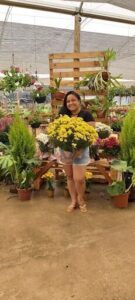 A woman is holding a yellow flower in front of a flower stand.