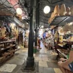 A woman is sitting in a market, looking at her cell phone.