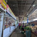 A woman is standing in front of a produce stand, selling vegetables.
