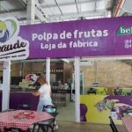 A woman is standing in front of a purple sign that reads "Polpa de Fructas" in white letters.