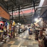 A woman walks down a hallway in a market, surrounded by various items for sale.