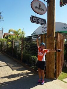 A woman wearing a bicycle helmet and an orange shirt is standing in front of a wooden pole with a sign on it.