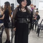 A woman wearing a black dress and a black hat poses for a picture.