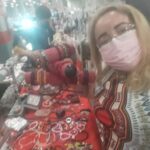 A woman wearing a mask is standing in front of a table full of beads and jewelry.