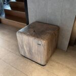 A wooden stool with a hole in the middle sits on a tile floor.