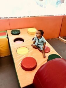 A young boy sits on a red and yellow pizza-shaped play mat.