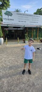 A young boy wearing green shorts and a white shirt is giving a thumbs up.