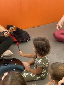A young girl is sitting on the floor, playing a drum.