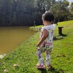 A young girl wearing a dress stands on the grass near a pond.