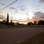 The sun is setting over a field, casting a warm glow on the landscape.