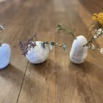 Three white rocks with purple flowers and greenery in between them.