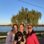 Three women pose for a picture in front of a tree, with one of them holding a baby.