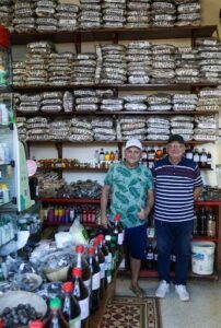 Two men pose for a picture in front of a store with a large display of bottles.