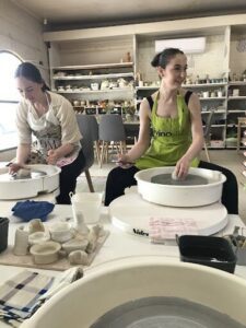 Two women are sitting at a table, working on pottery.