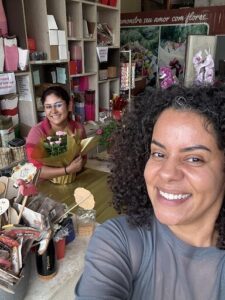 Two women are smiling and posing for a picture in front of a flower shop.