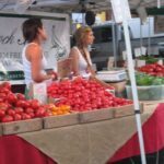 Two women are standing in front of a table full of tomatoes.