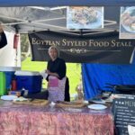 Two women are standing in front of a tent, which is advertising Egyptian styled food.