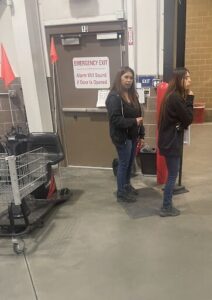 Two women standing in front of a door with an emergency exit sign.