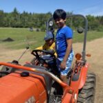 Two young boys are sitting in a tractor, enjoying the ride and the outdoors.