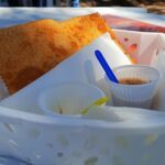 A basket of food with a blue plastic spoon in it.