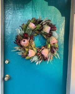 A beautiful blue door with a wreath of flowers and leaves.