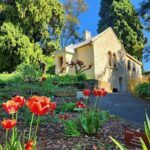 A beautiful garden with a white house in the background, featuring a variety of flowers, including red tulips.