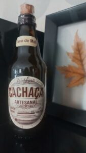 A bottle of Caciquinha sits on a table next to a leaf.