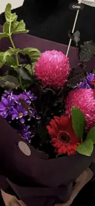 A bouquet of flowers in a box, including a pink flower, a purple flower, and a red flower.