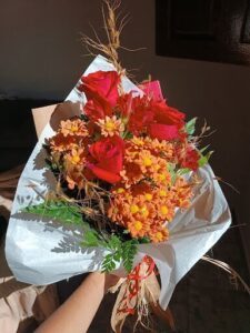 A bouquet of flowers is held in a hand, with a red ribbon tied around it.